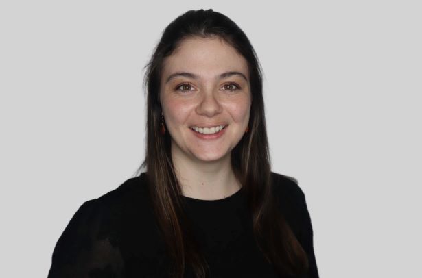 Professional headshot of a smiling woman with long dark hair, wearing a black top against a light background